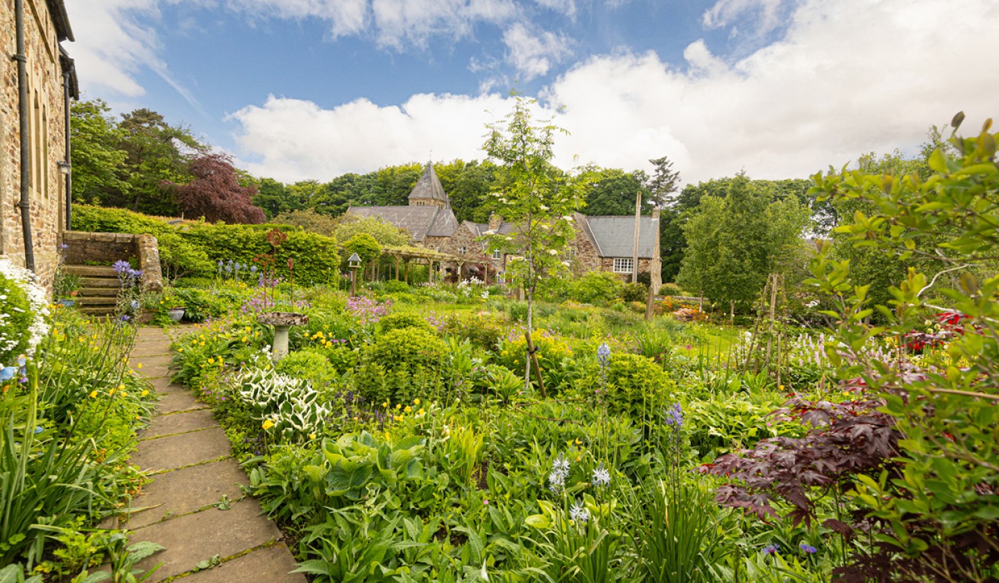 Well kept garden full of plants with a pathway alongside the house